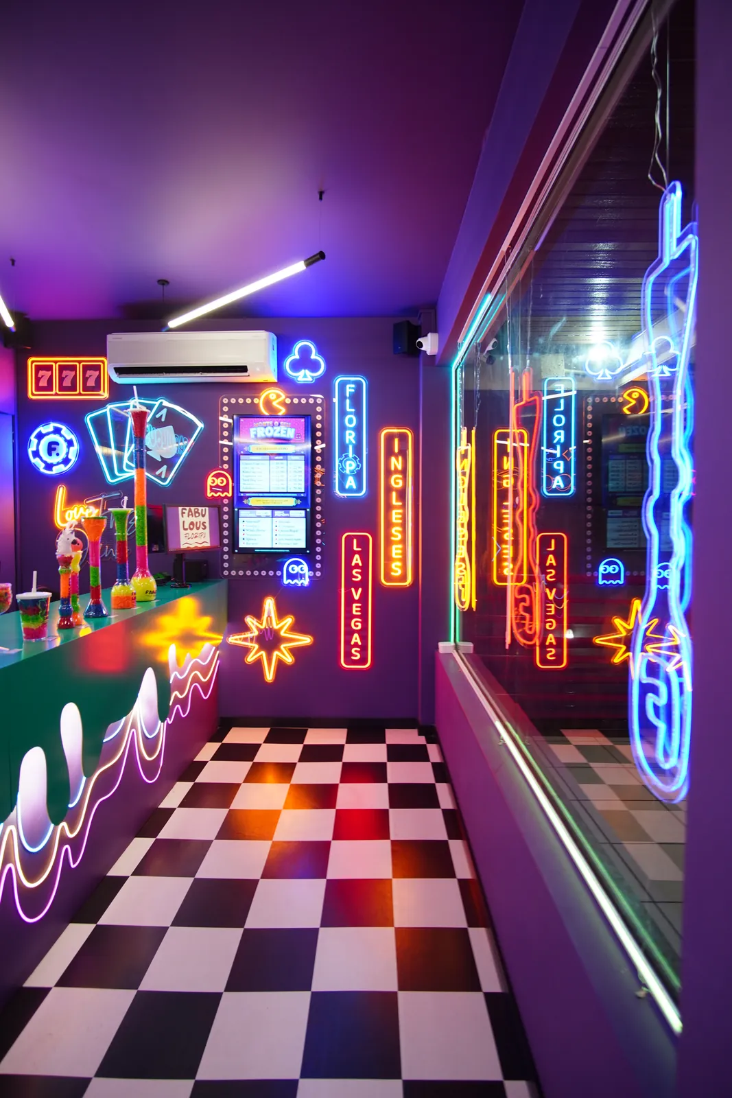 Balcão de atendimento do Fabulous, com piso xadrez, parede roxa e letreiros de neon